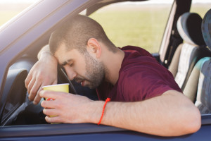 tired unshaven male leans on wheel and holds paper cup of coffee